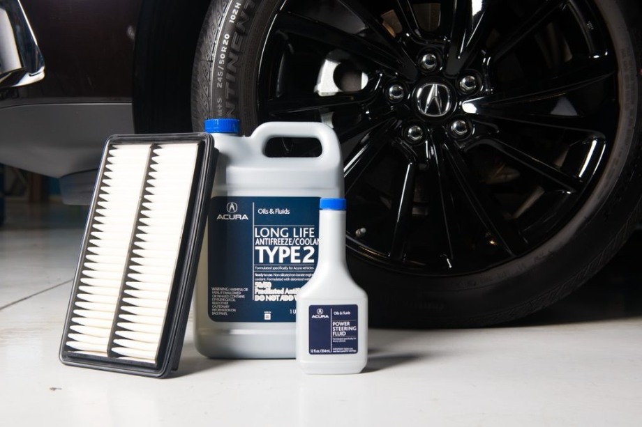Acura service center materials on the ground including a filter, a container of antifreeze/coolant, and power steering fluid.
